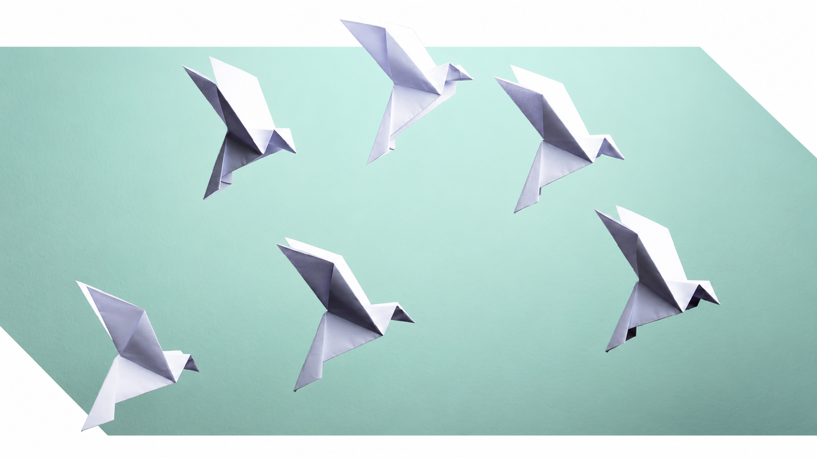 Origami paper birds flying against a mint green background